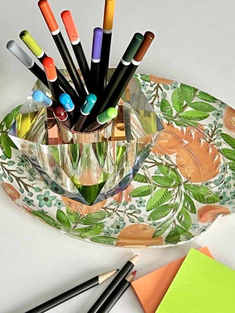 A decoupage glass plate used as a desk accessory to hold colored pencils.