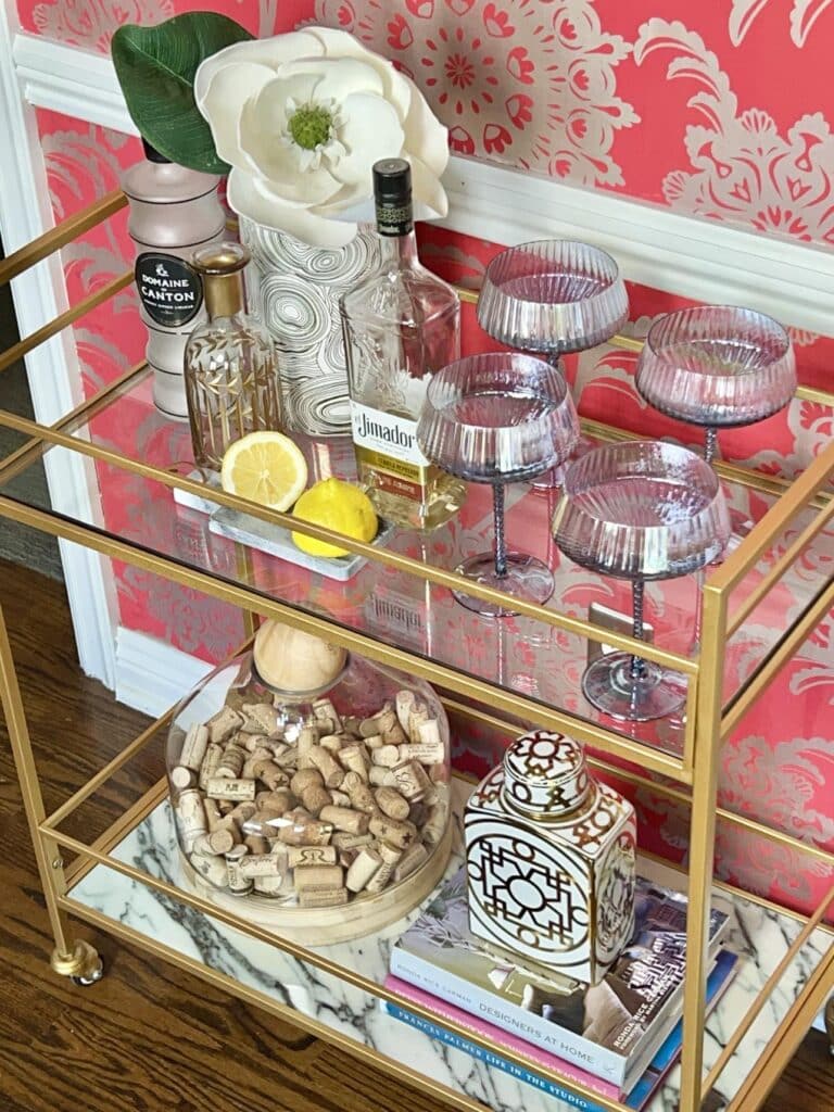 A glamorous bar cart styled with crystal glasses, gold and white vases, and unique liquor bottles.