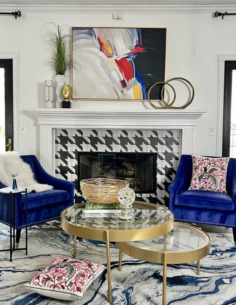 Glamorous decorating ideas include a red, blue, and yellow abstract wall art piece, velvet chairs, gold and glass accents, and embroidered pillows.