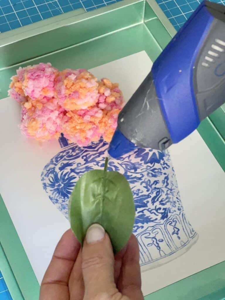 Hot gluing faux green leaves to the artwork.