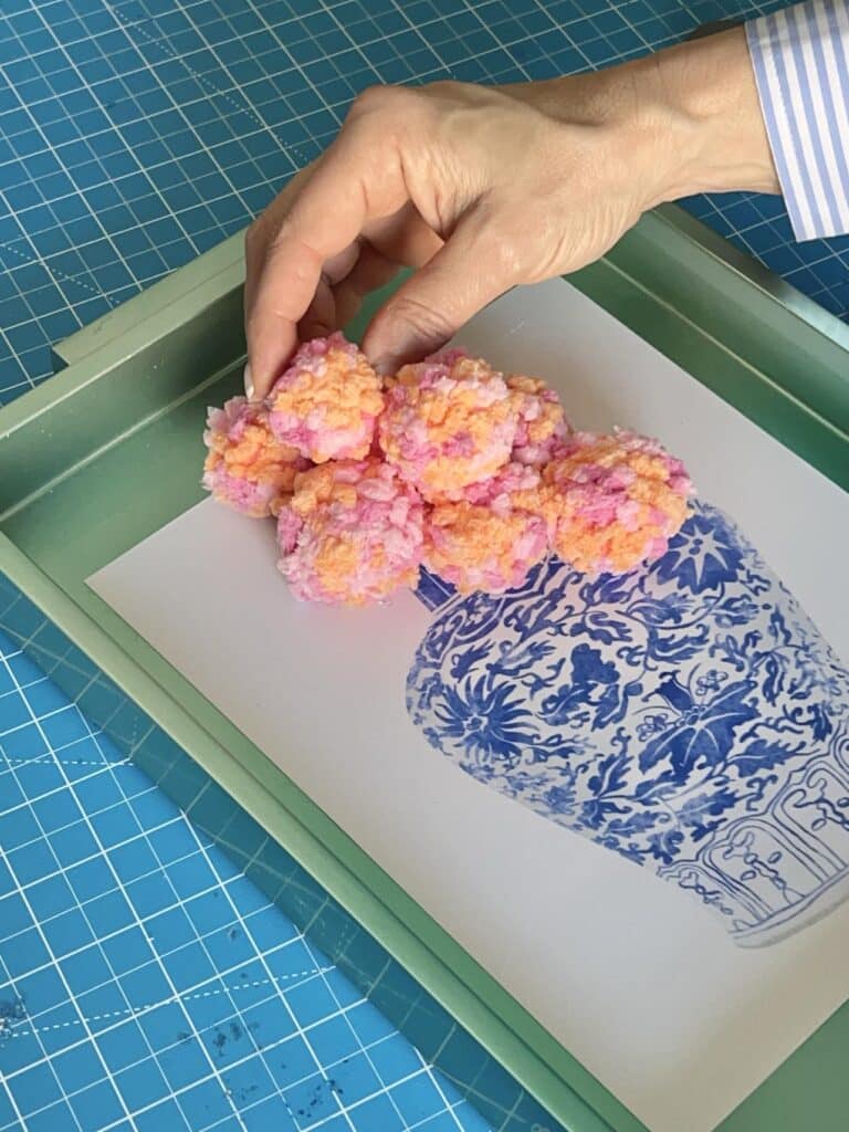 Gluing a seconde layer of poms onto the art print to create 3D dimension on the yarn wall decor diy.