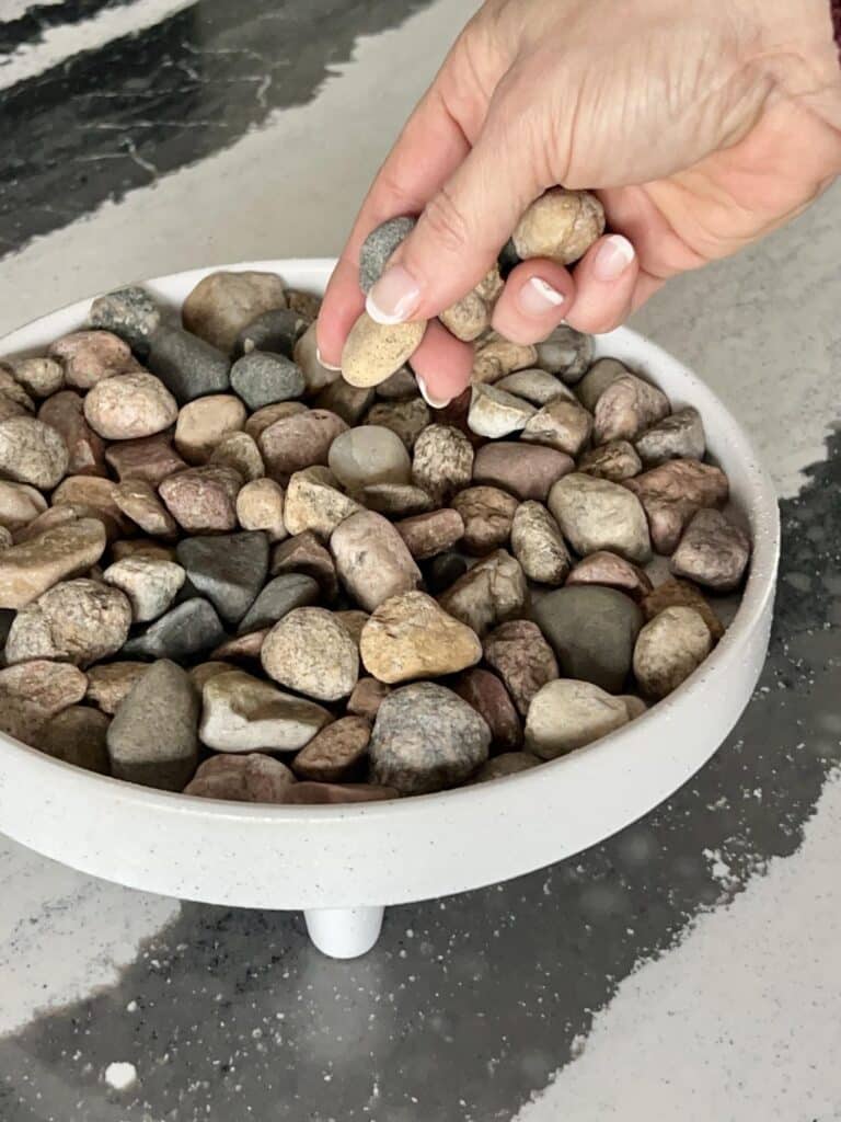 Adding river rock to a container for a pebble tray for plants.