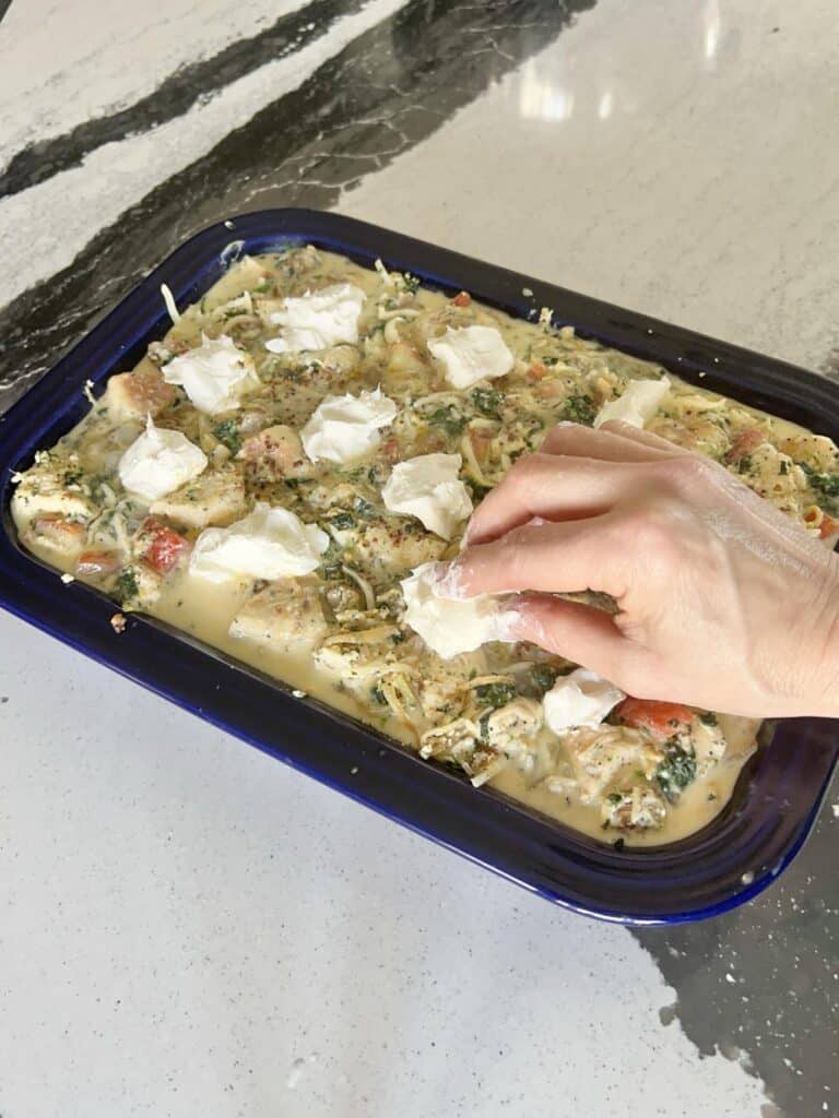 Placing cream cheese chunks into the top of the everything bagel casserole.