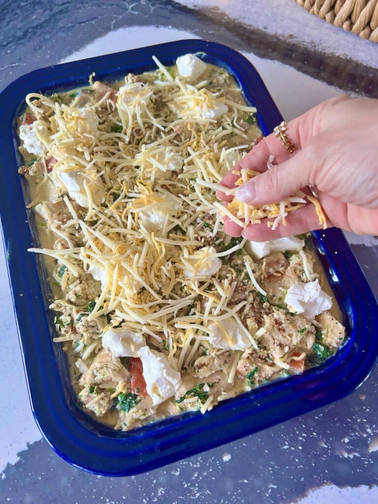 Adding shredded cheese to everything bagel casserole before baking.