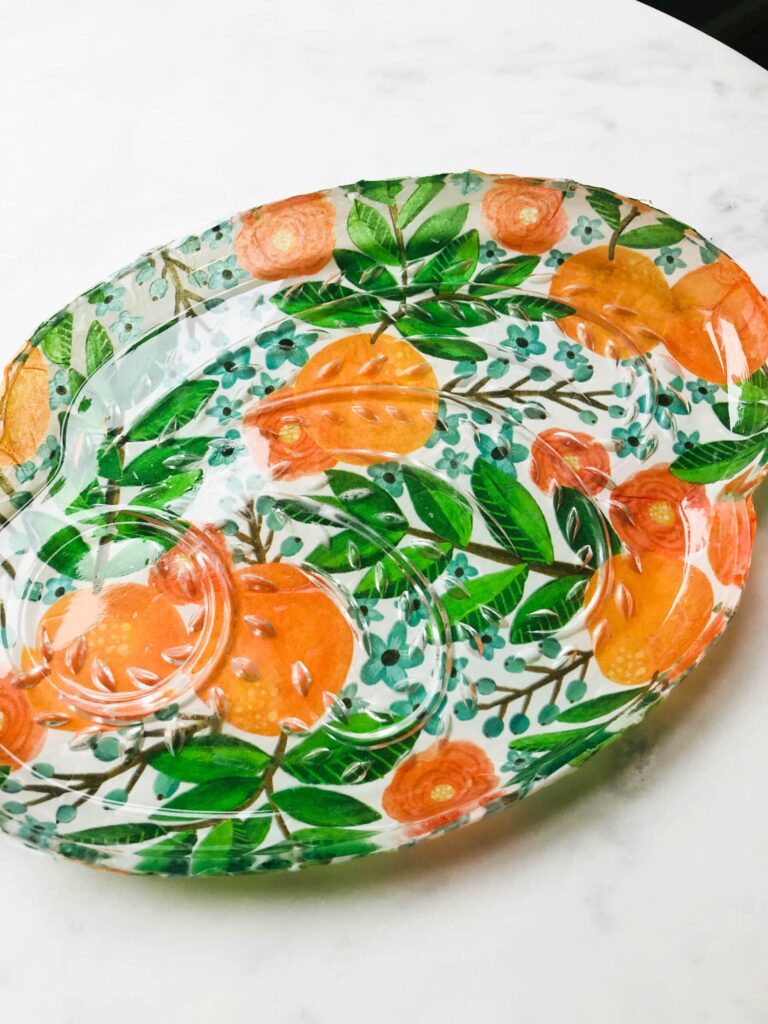 A completed decoupage glass plate using orange and green tissue paper.