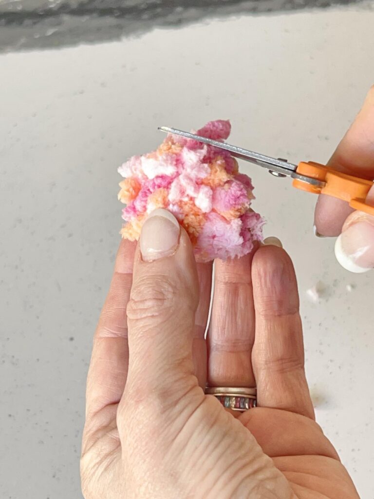 Trimming a pom pom with scissors for a yarn wall decor diy.