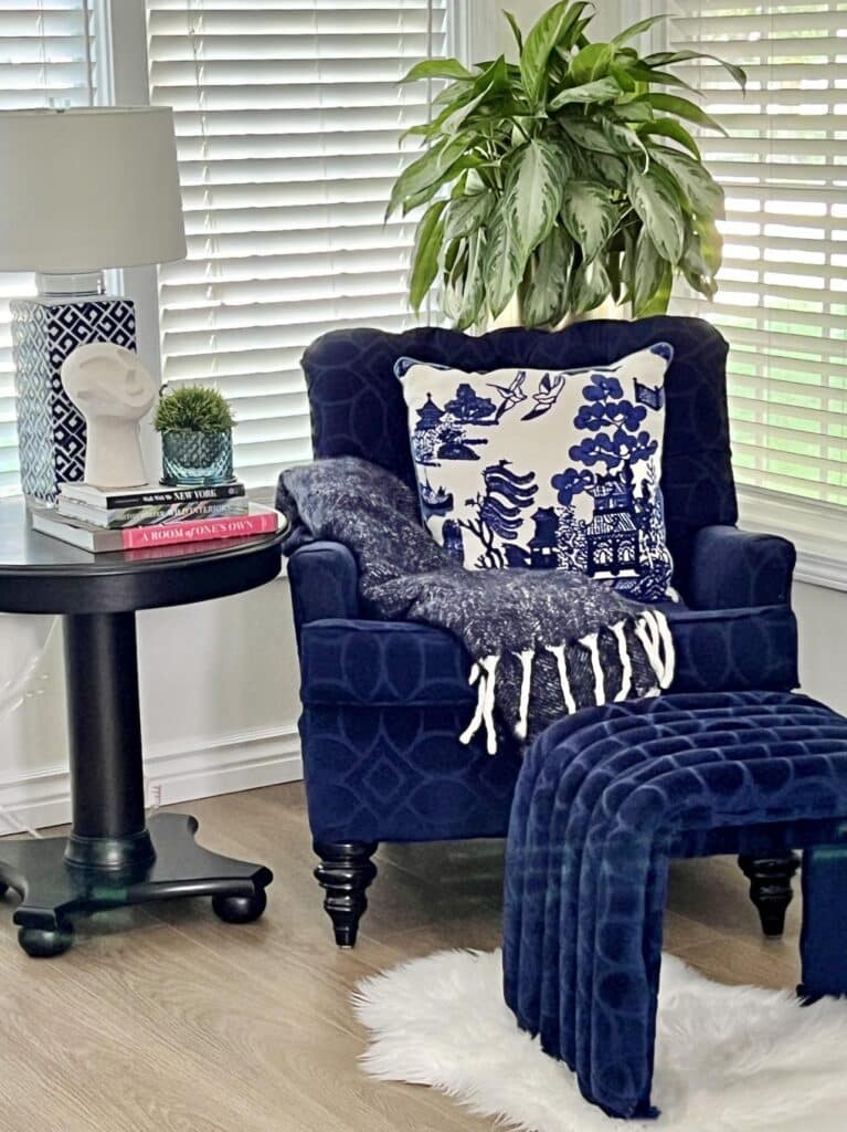 A reading nook with a side table, a chair, and a diy upholstered ottoman made from pool noodles.