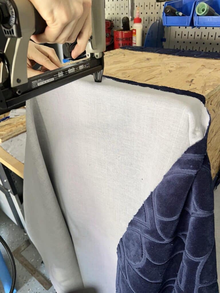 Stapling fabric onto a diy ottoman frame.