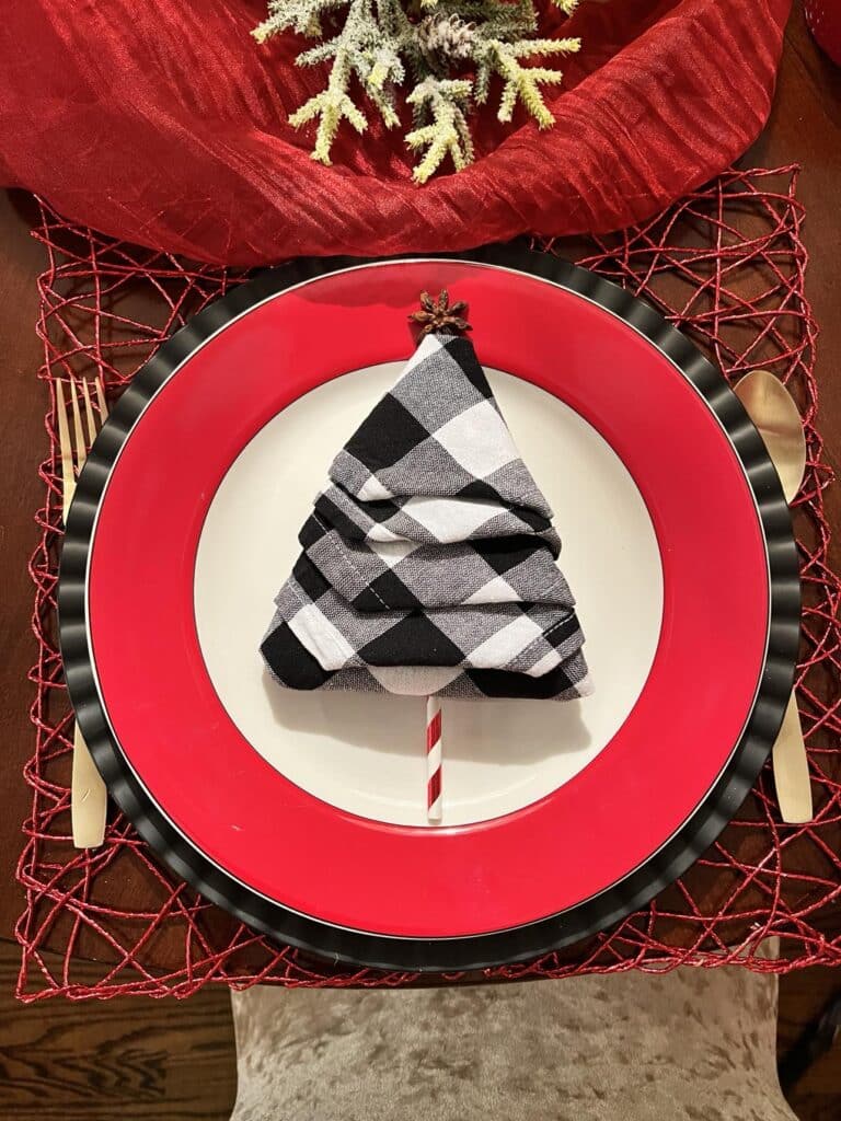 A black and white buffalo check cloth napkin folded into the shape of a Christmas tree.