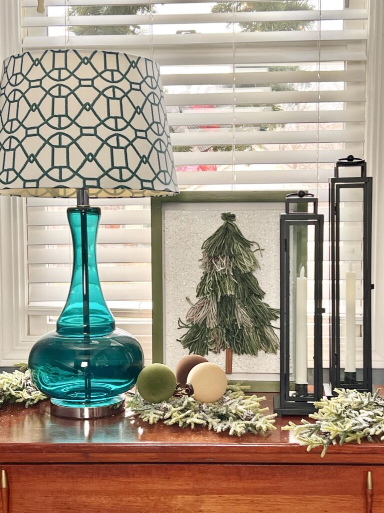 DIY Christmas tree tassel artwork displayed beside a bedroom lamp.