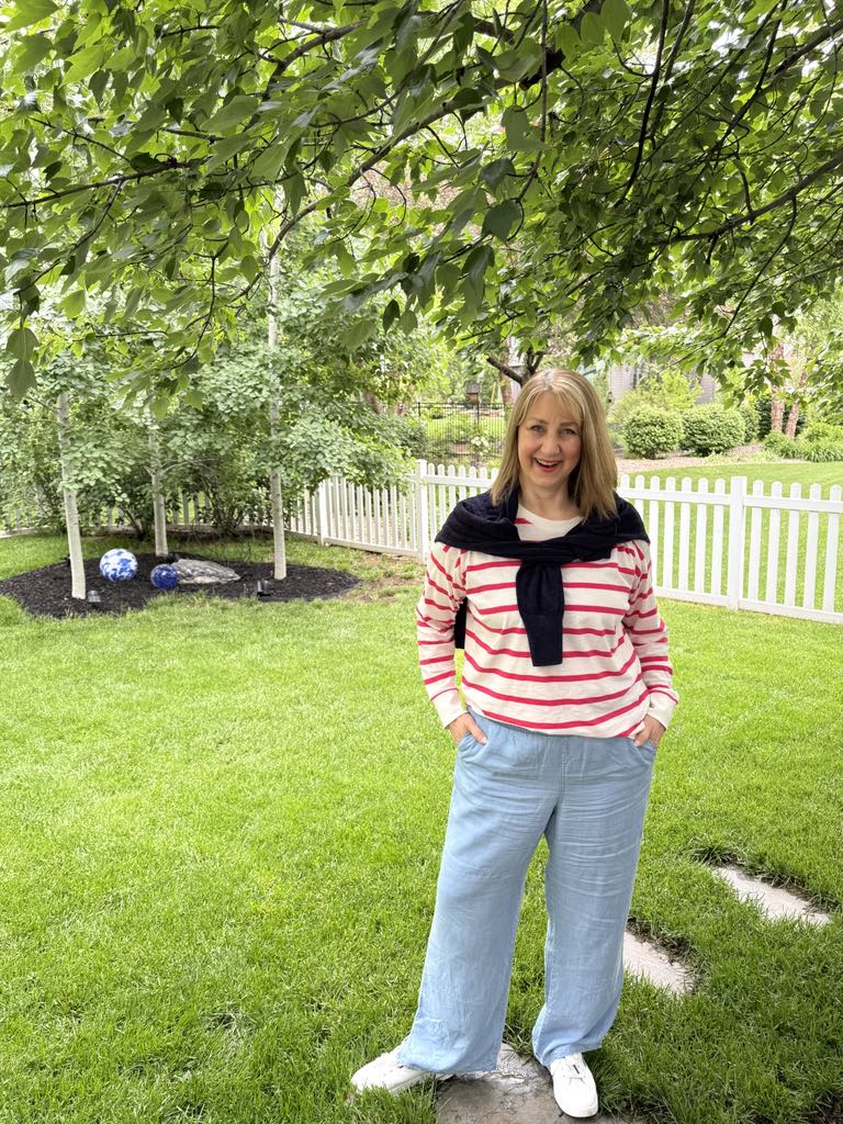 how to dress preppy: Woman wearing pink and ivory striped shirt with blue sweater tied over her shoulders.
