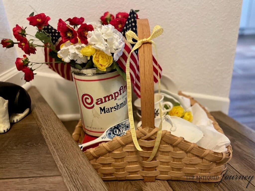 A woven basket with a vintage marshmallow tin filled with yellow and white flowers.