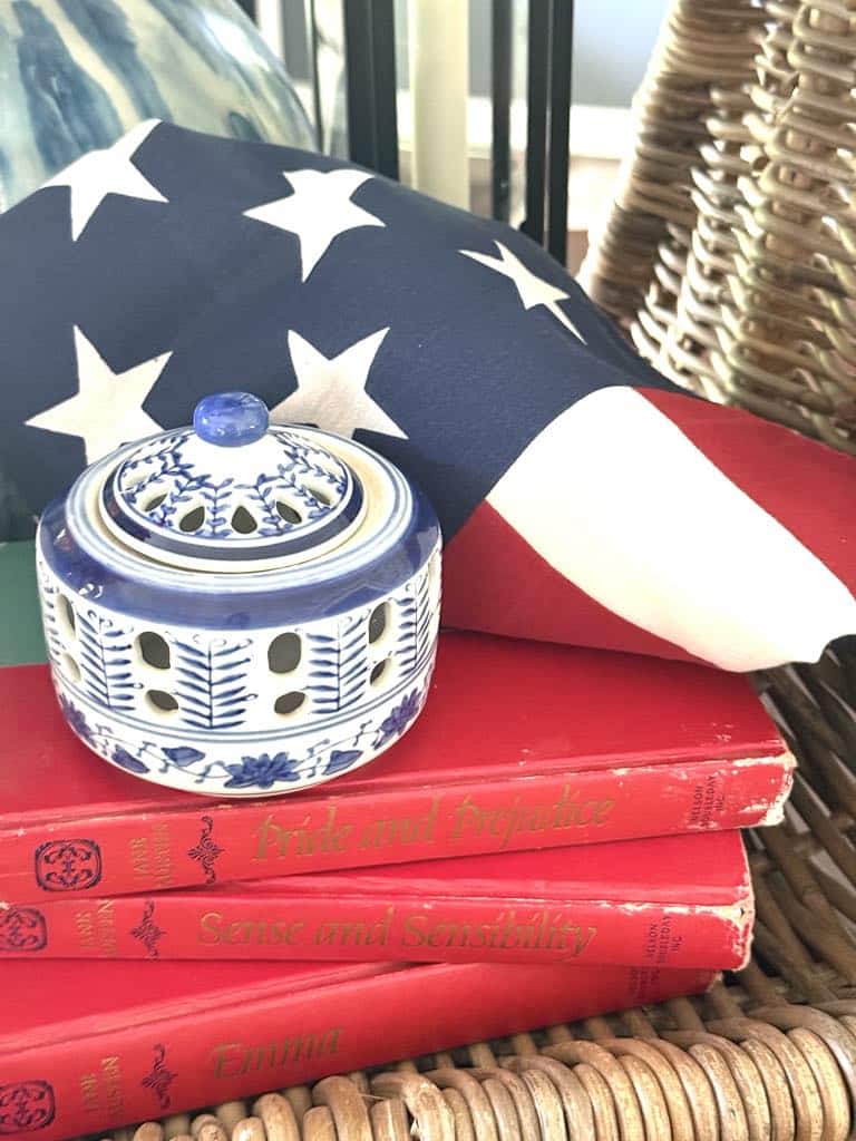 An American flag folded and displayed on top of a stack of books and beside a blue and white chinoiserie vase for a patriotic centerpiece.
