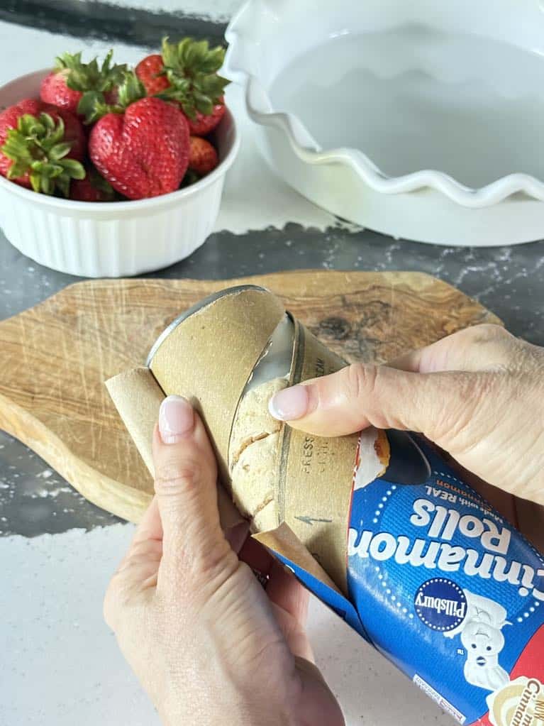 Opening tube of refrigerated cinnamon rolls.