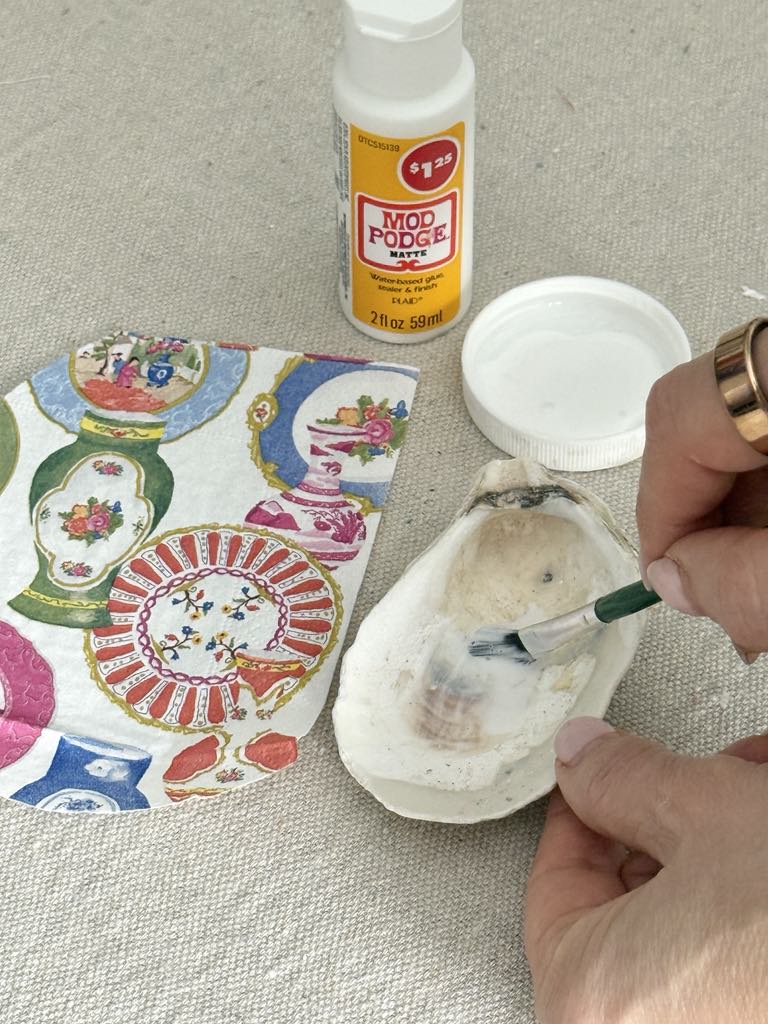 Brushing a thin layer of decoupage glue onto the inside of oysters shells.