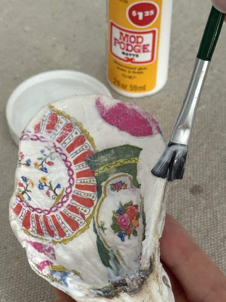 Brushing decoupage glue onto the edge of an oyster shell.