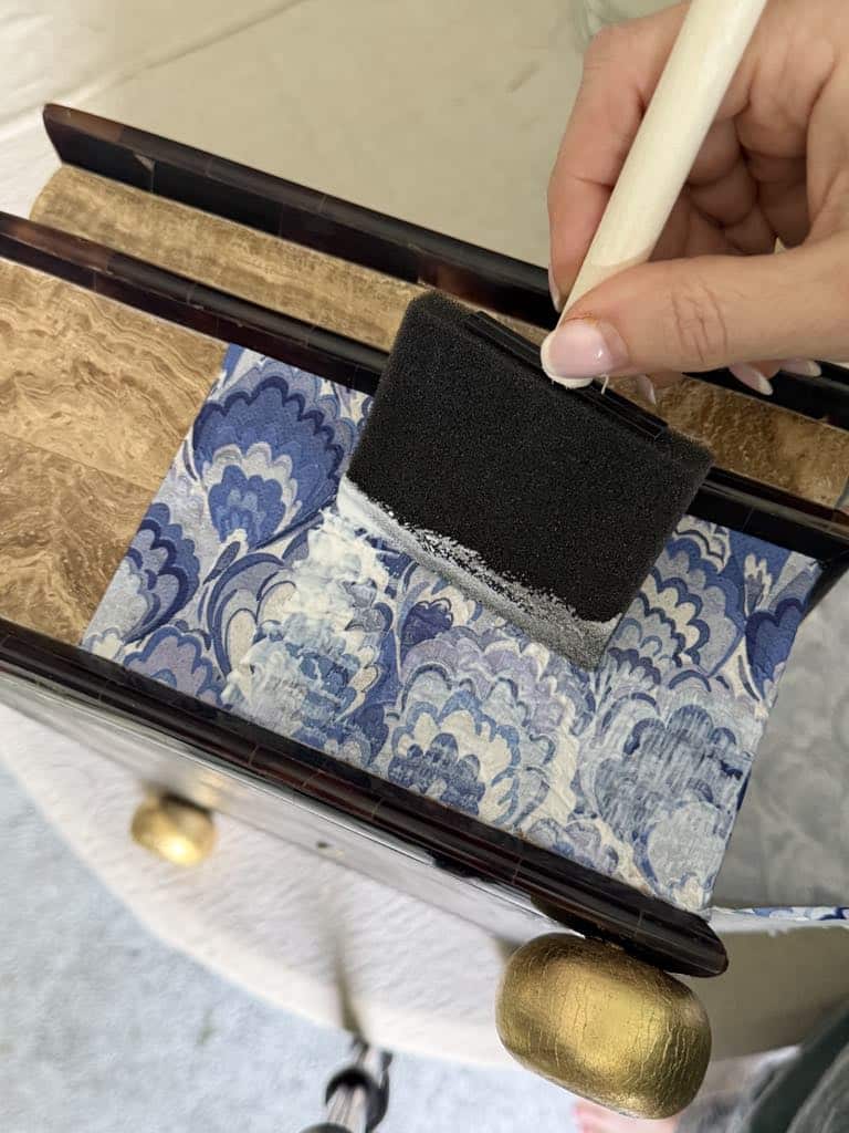 Sealing a napkin to a box with decoupage glue.