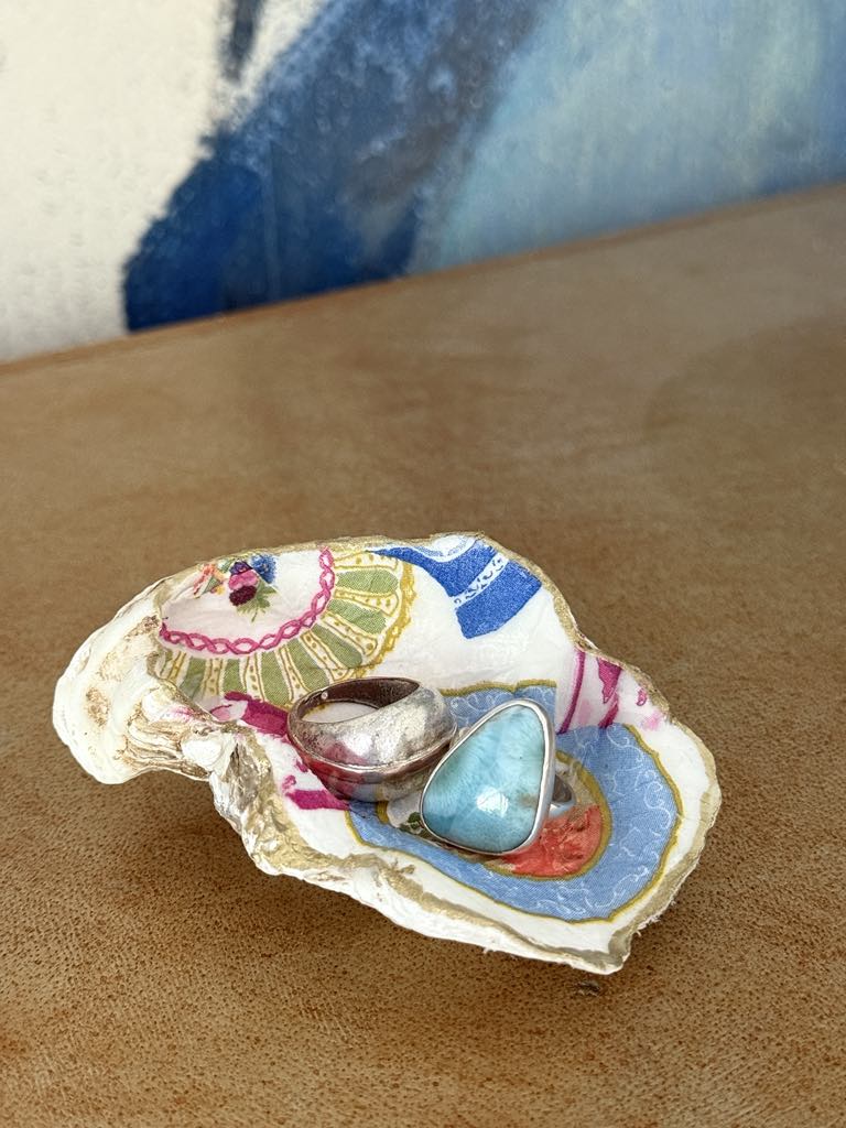 A decoupaged oyster shell used as a trinket holder with two rings inside.