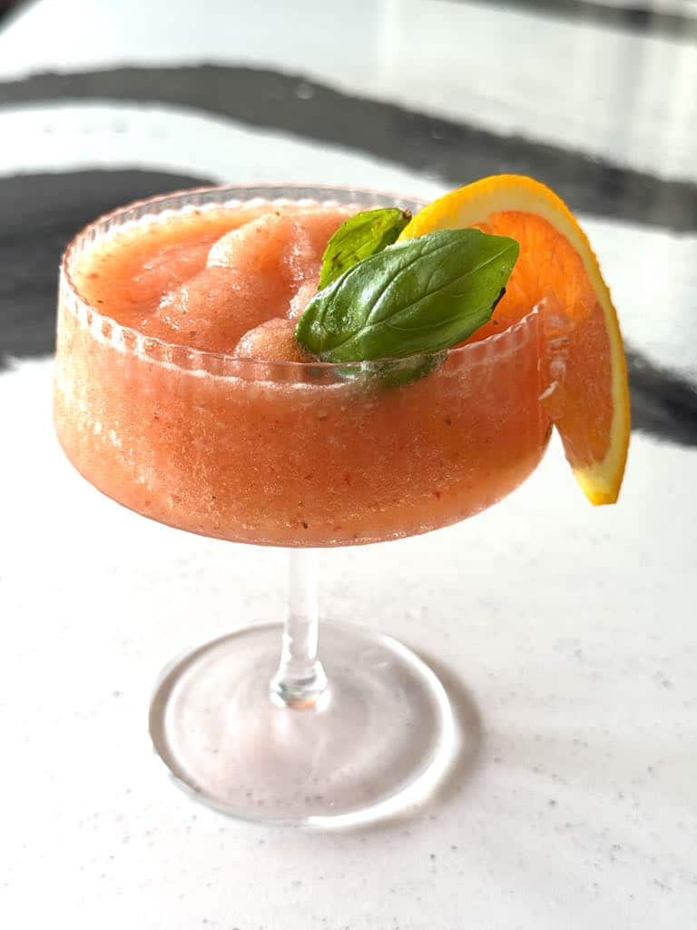 A frozen aperol spritz with orange slice and basil leaf.