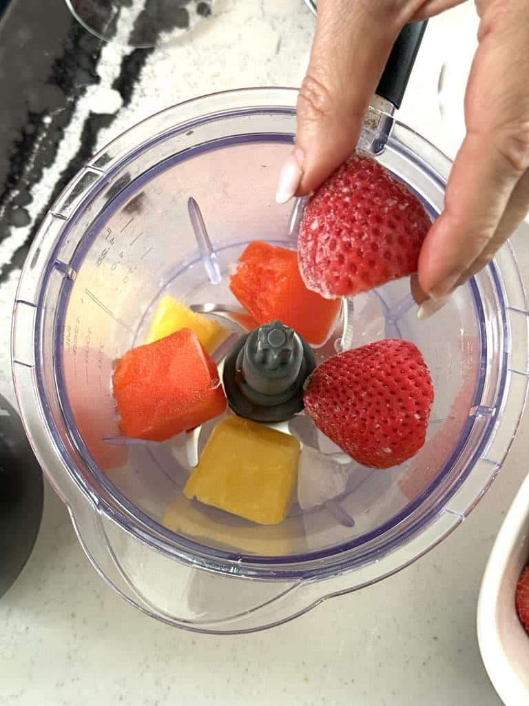 Placing frozen strawberries, orange juice, and aperol into food processor.