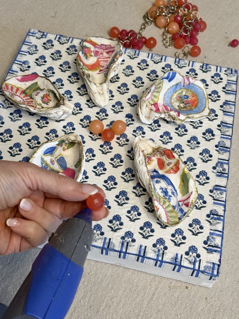 Gluing color beads to the middle of a decoupaged canvas surrounded by decoupage shells.