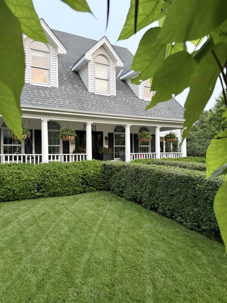 A green hedge leading up to the front porch of a white house.