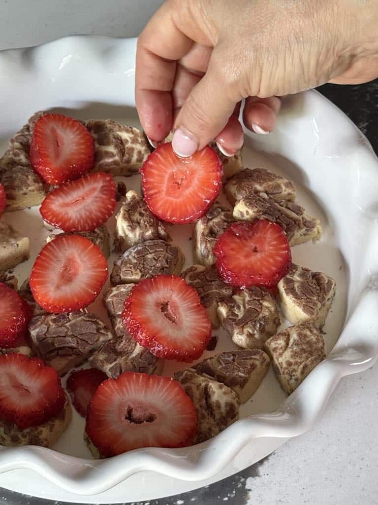 Layering strawberries on top of cinnamon roll pieces for breakfast casserole.