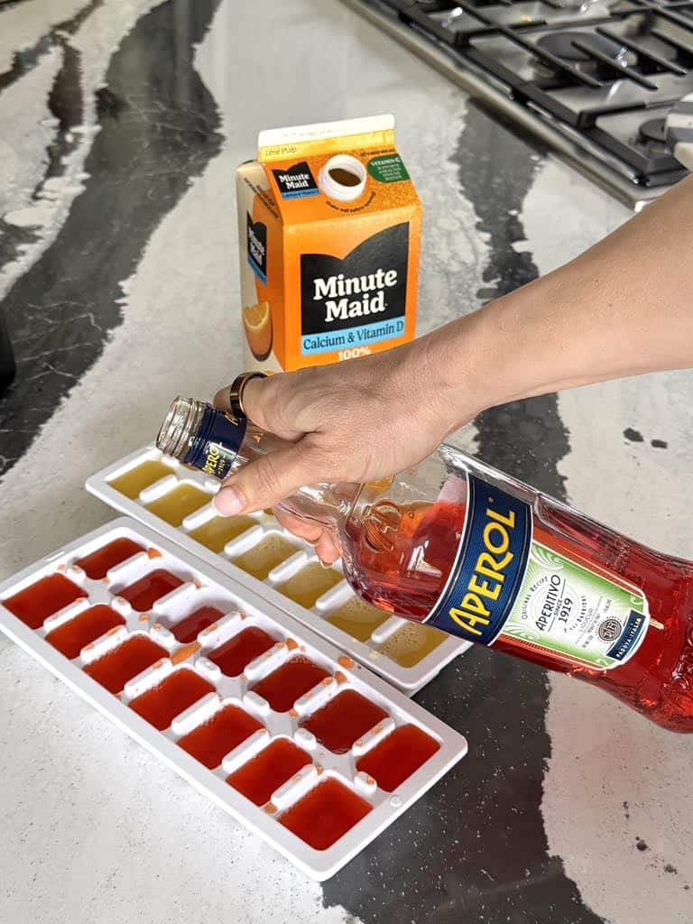 Pouring aperol into ice cube trays.