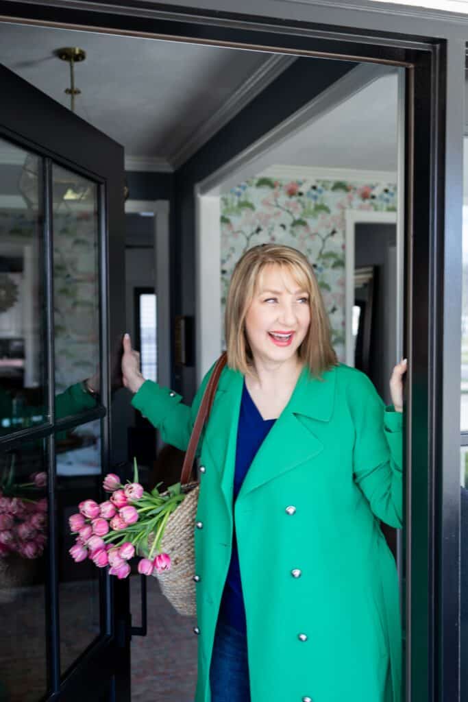 Woman in green coat opening a front porch door.