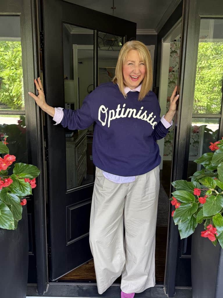 how to dress preppy: Woman wearing khaki pants and a navy blue sweater that spells the word "Optimistic" on the front.