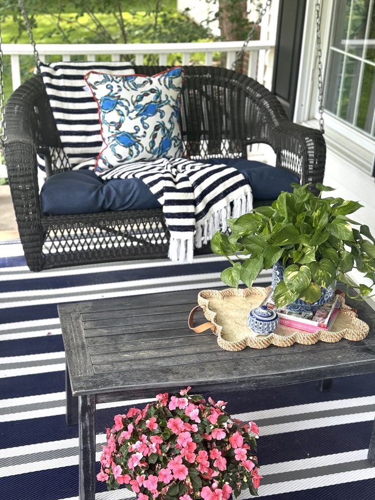 Front porch swing styled with an outdoor pillow, throw blankets, coffee table, and plants.