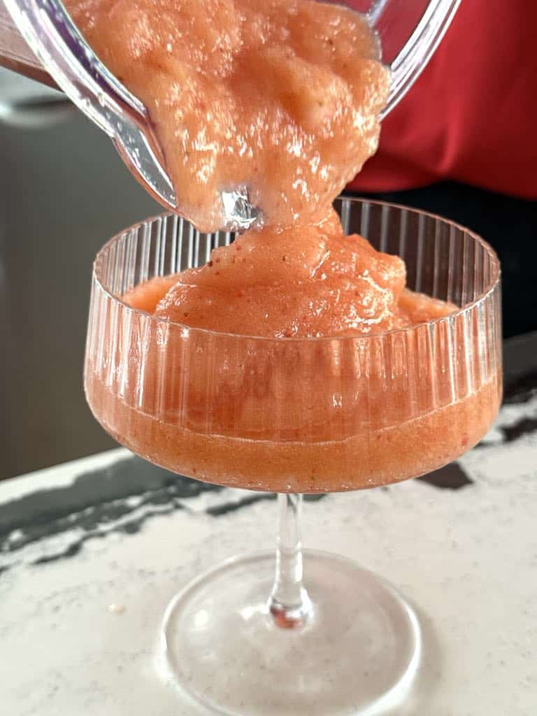 Pouring blended frozen aperol spritz into a coup glass.