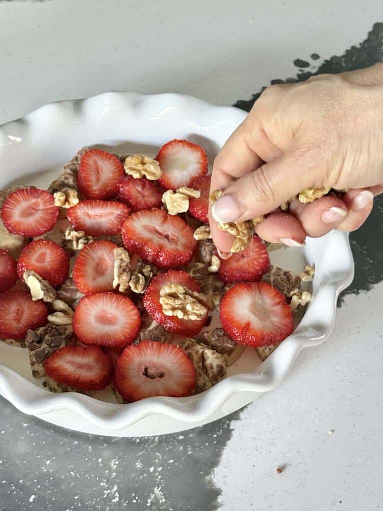 Sprinkling nuts on top of strawberry cinnamon roll casserole.