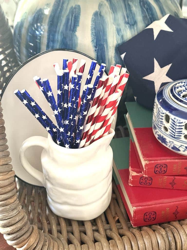 Patriotic straws in a small white pitcher styled beside a stack of books and an American flag.