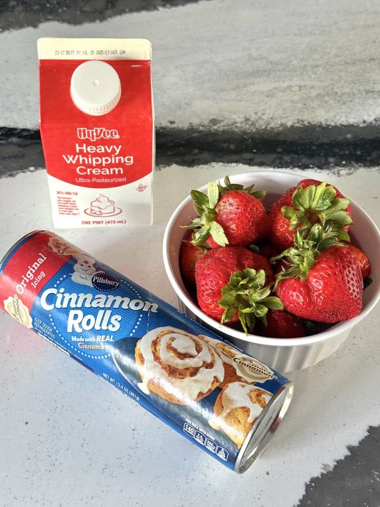 Ingredients for Strawberry Cinnamon Roll Casserole: tube of refrigrated cinnamon rolls, heavy whipping cream, and fresh strawberries.