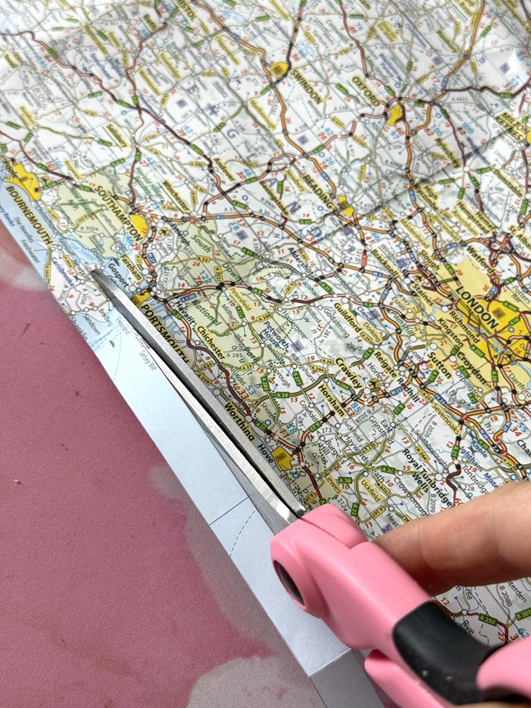 Cutting half inch strips of a map with scissors.