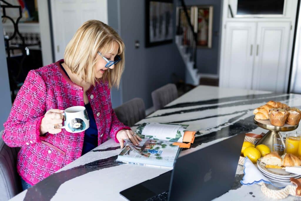 Woman holding a cup of coffee while reading a book in a kitchen.