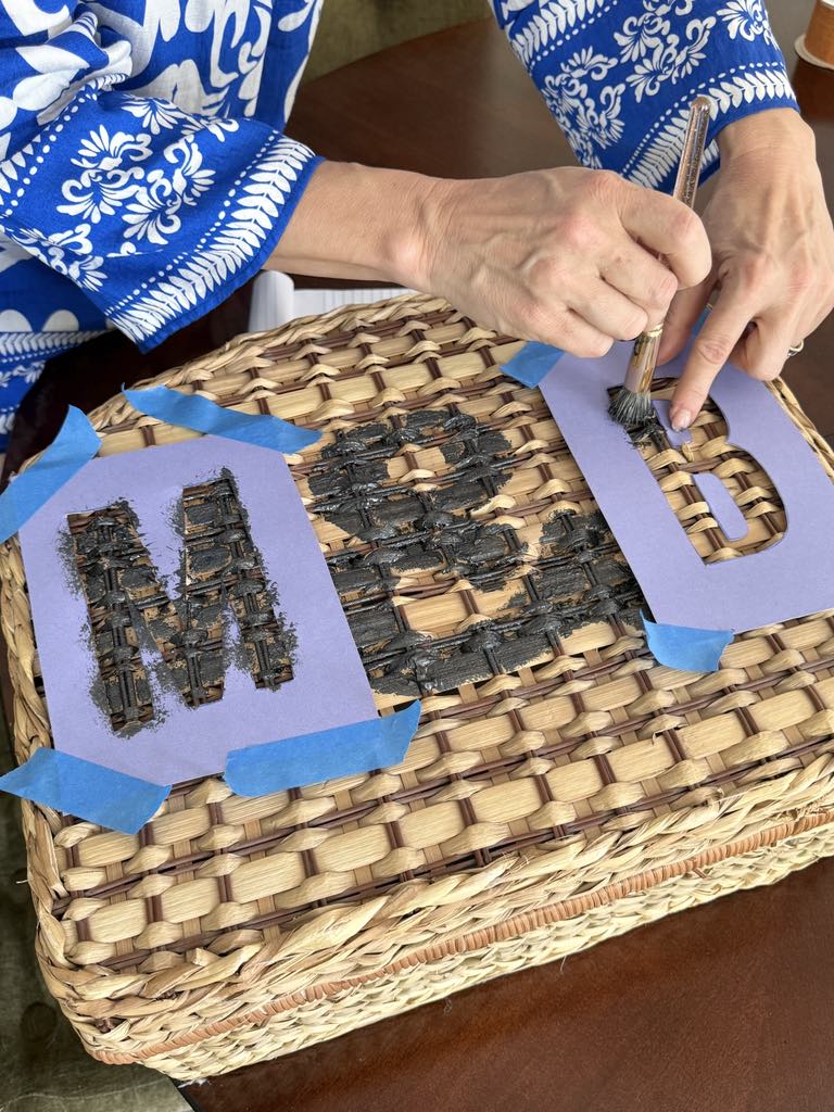 Painting a stencil on the top of a picnic hamper.