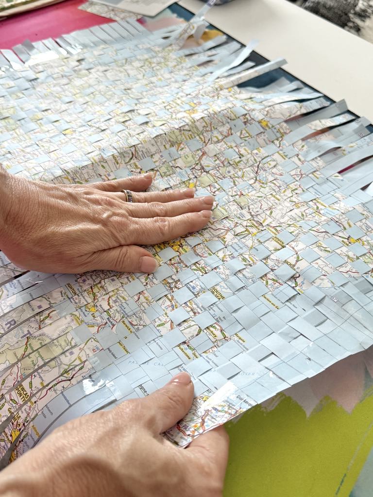 Woman pressing woven map strips onto outside of notebook for a DIY travel journal.