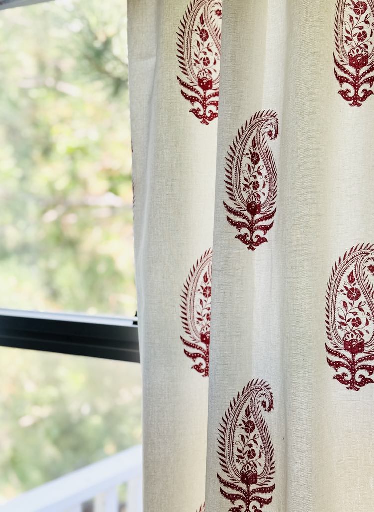 A red block print pattern decorating a cream curtain panel.