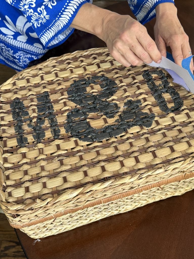 Removing the stencil after painting initials on a picnic basket.