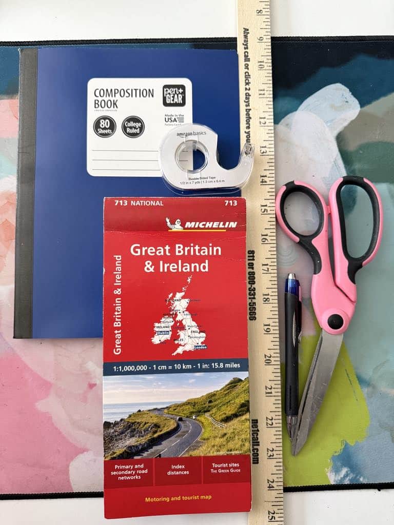 A blue notebook, a red map of England, tape, ruler, scissors, and pen.