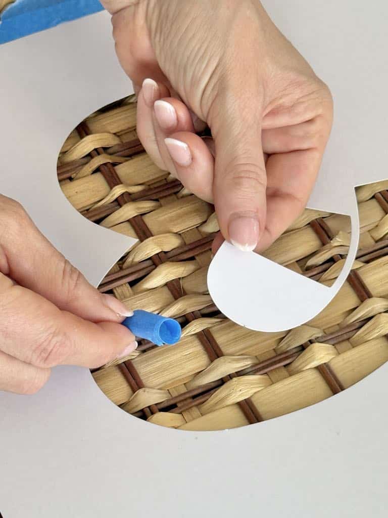 Taping an "&" stencil to the top of a basket.