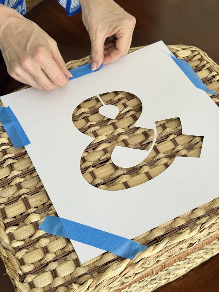 Taping a stencil to the top of a picnic basket.