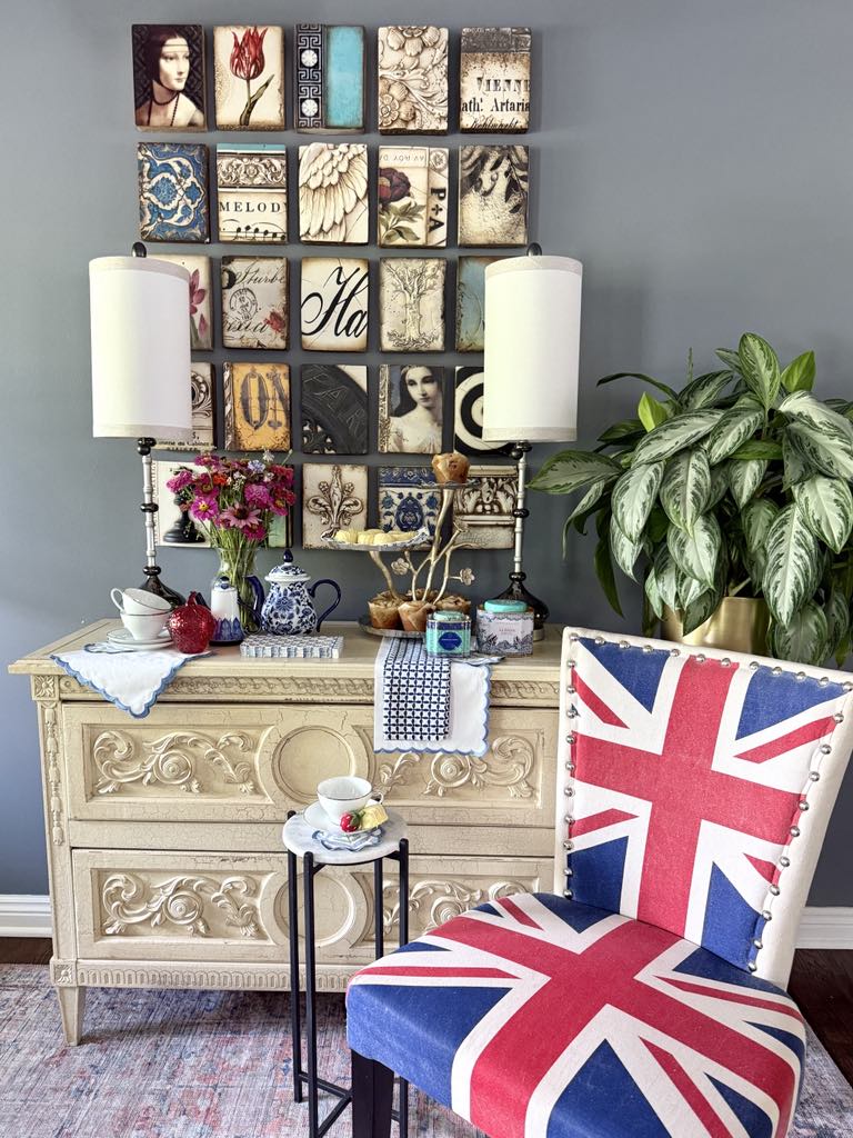 A tea party tablescape with a tiered tray, scalloped linens napkins and an upholstered chair with a Union Jack flag pattern.