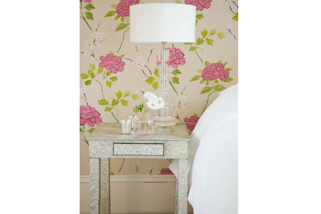 A nightstand styled with a clear acrylic lamp and a bud vase filled with fresh flowers.