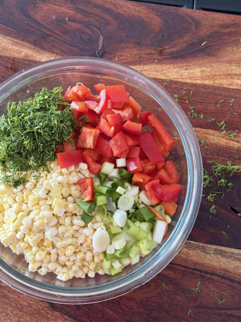 A bowl of fresh corn, green onion, fresh dill, and red pepper.