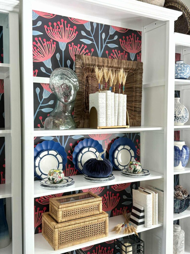 A bookcase styled with plates, pumpkins, and books.