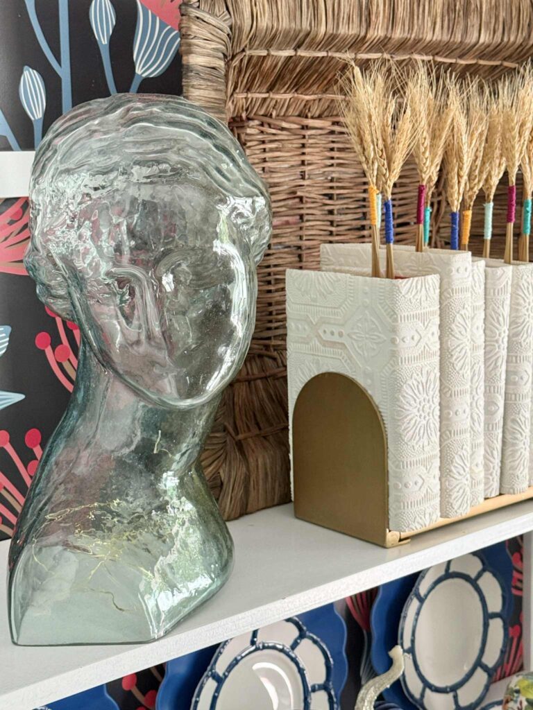 A glass bust sitting on a bookshelf beside books with DIY book covers.
