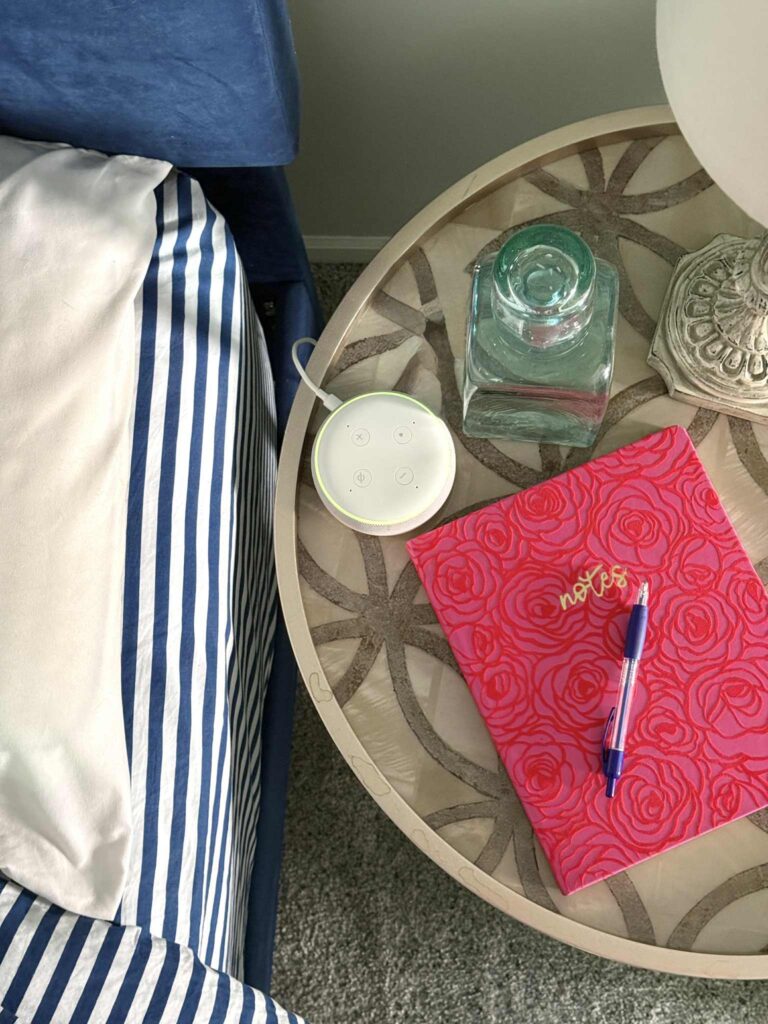 A nightstand with a journal, pen, Alexa, and bottle of water.